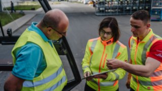 Drei Personen mit Warnwesten im Gespräch: Sicherheitsberatung vor Ort beim Kunden.